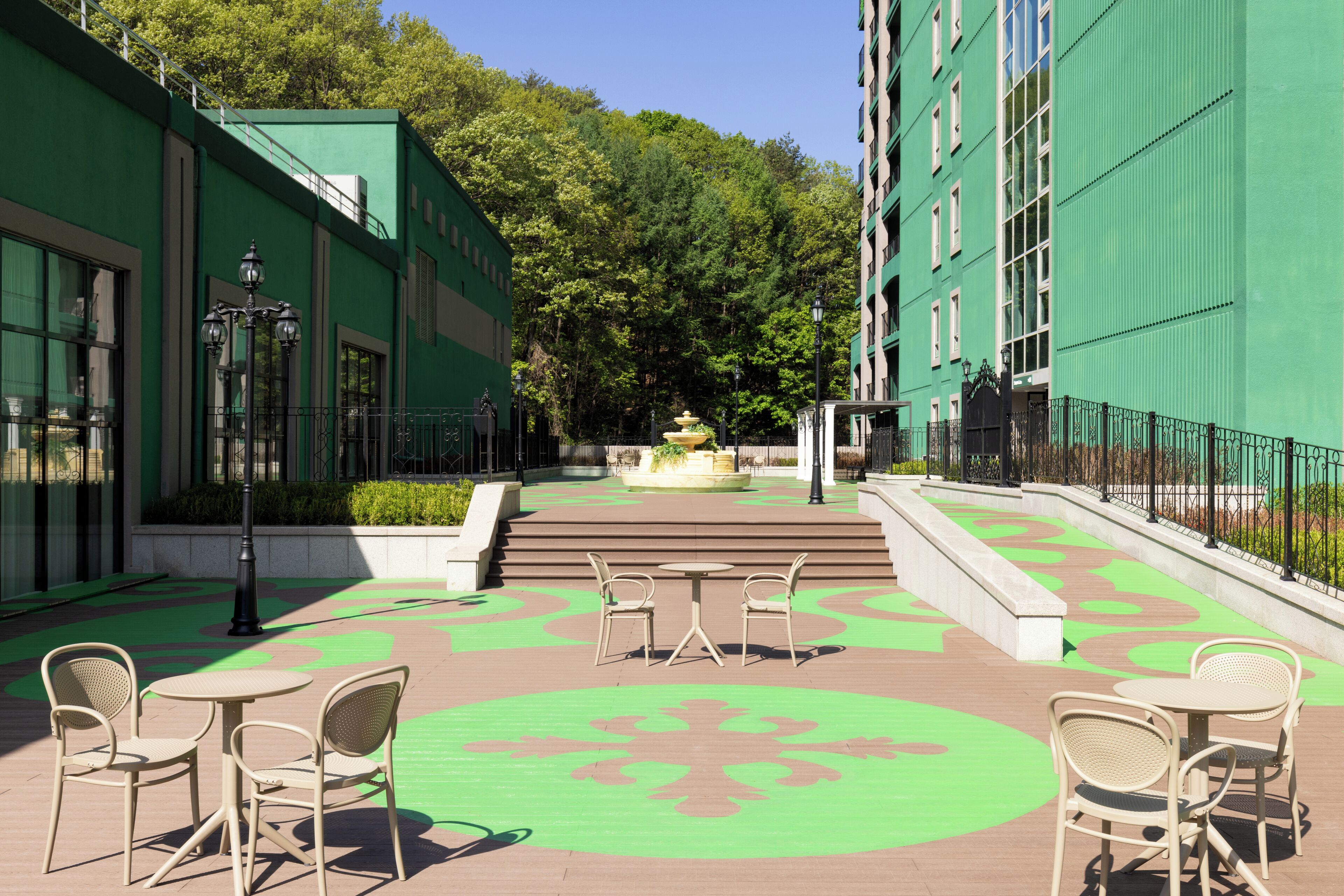 Un patio con paredes de color verde, una fuente y mobiliario exterior.