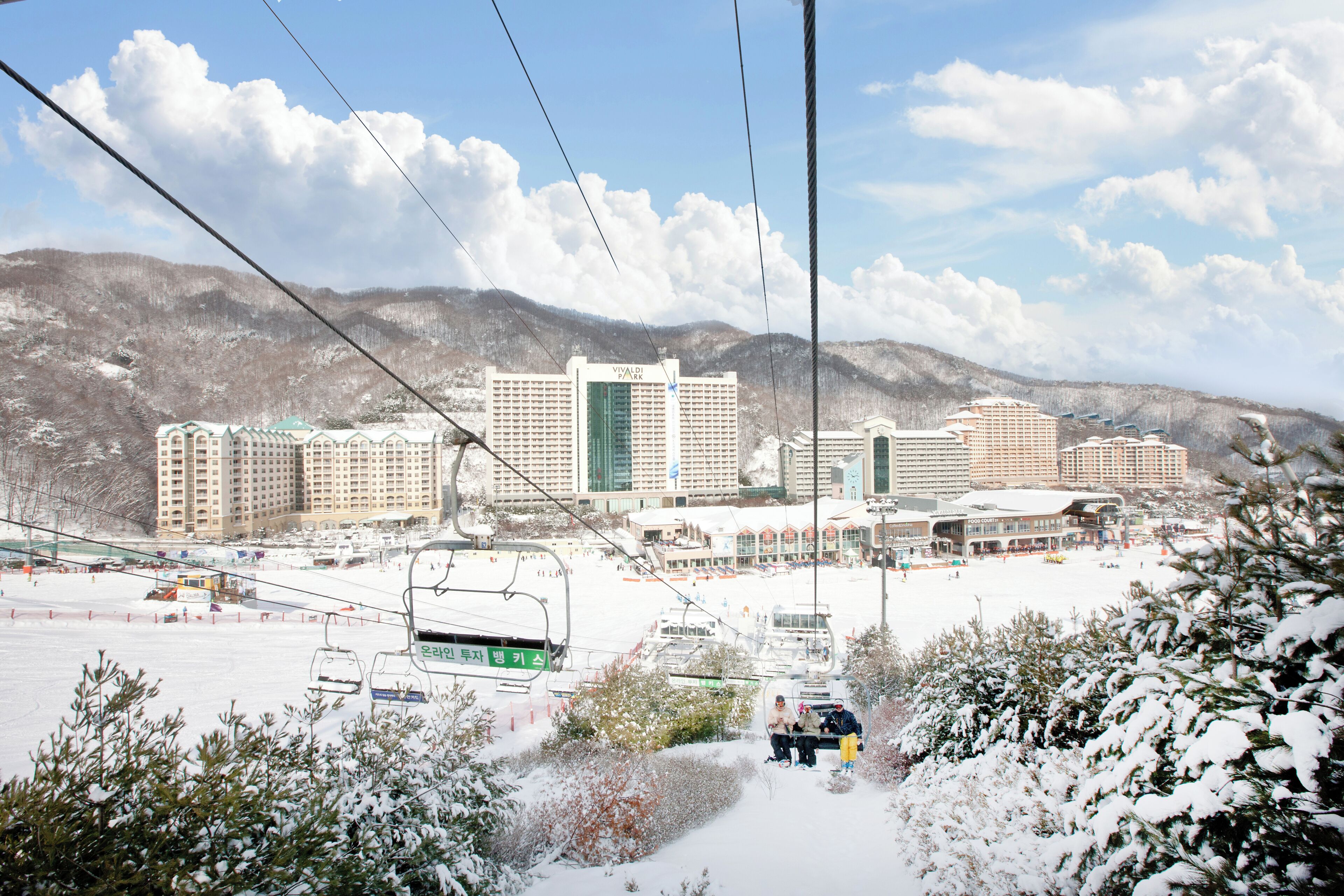 A snow-covered ski resort with multiple buildings, including a prominent hotel with a green and white facade.
