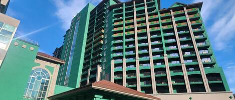 Un edificio alto con múltiples balcones, un llamativo frente verde y un cielo azul despejado al fondo.