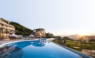 Un hotel moderno con piscina, campo de golf y montañas al fondo.