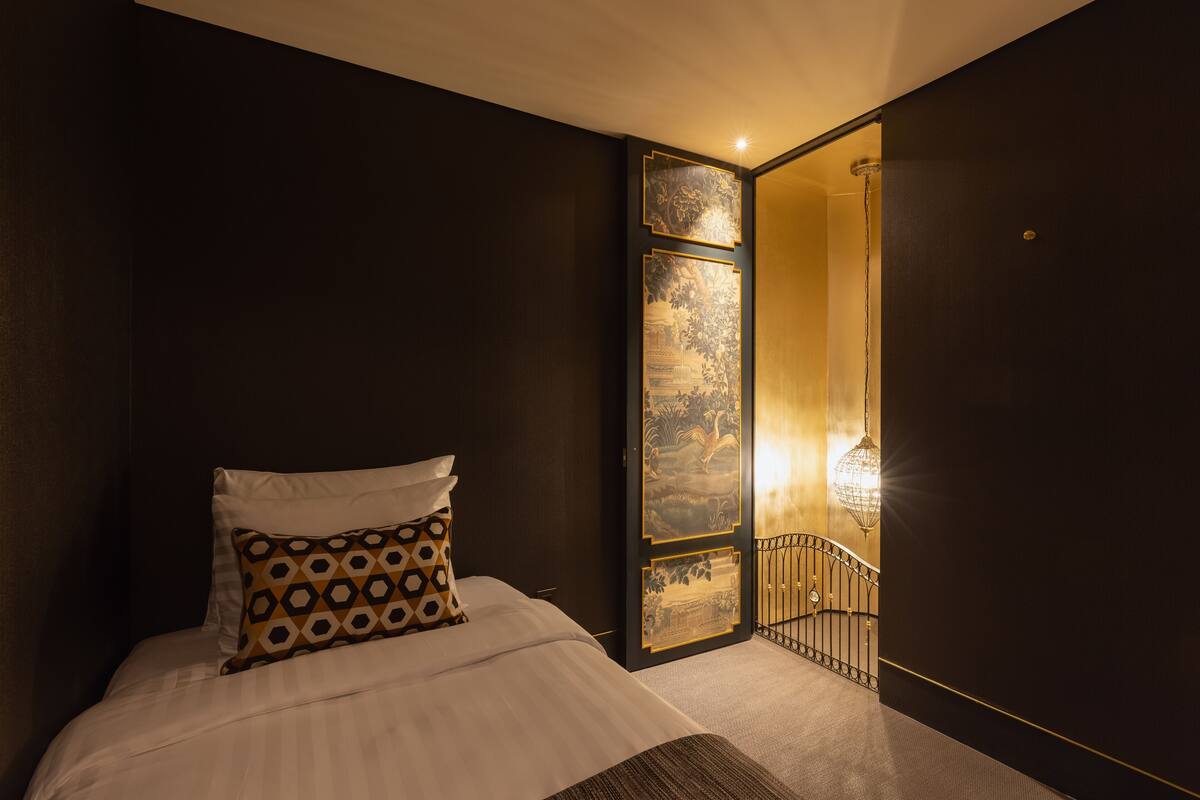 A hotel room with a bed, a patterned pillow, a wall with artwork, and a staircase leading to a balcony.