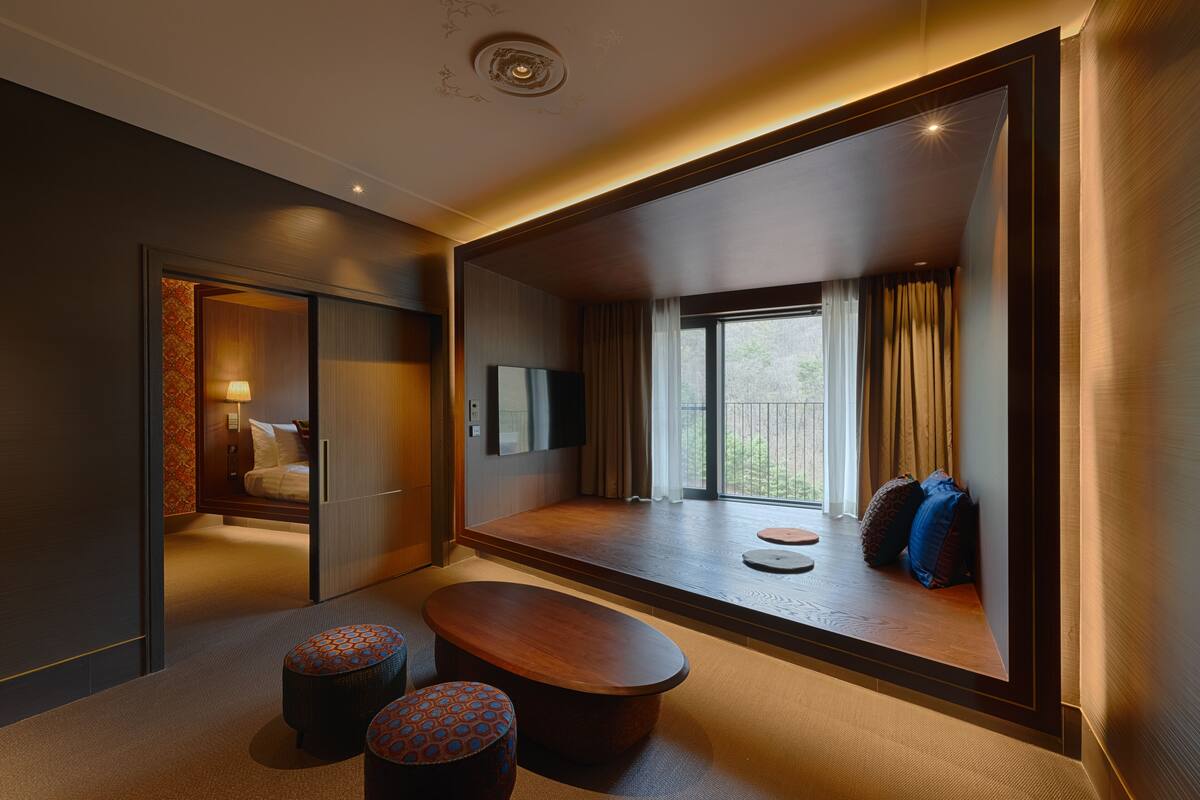 A modern hotel room with a large window, a flat-screen TV, a sofa, and a wooden coffee table.