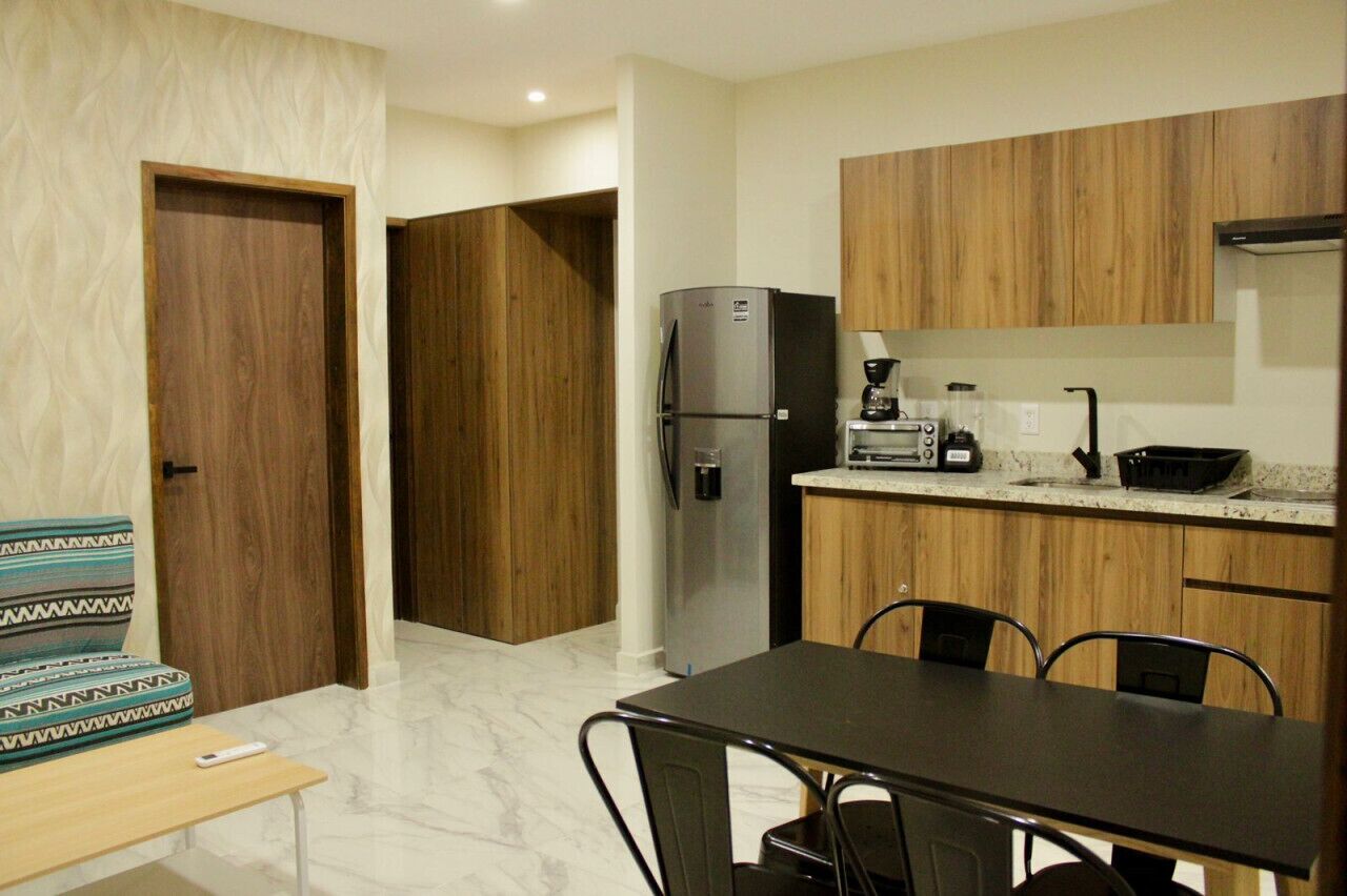A compact kitchen with wooden cabinets, a refrigerator, a coffee maker, and a dining table with chairs.