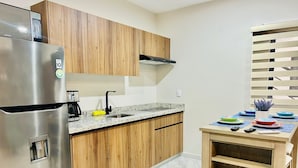 Una cocina moderna con armarios de madera, un refrigerador de acero inoxidable, un horno empotrado y una pequeña mesa de madera con vajilla.