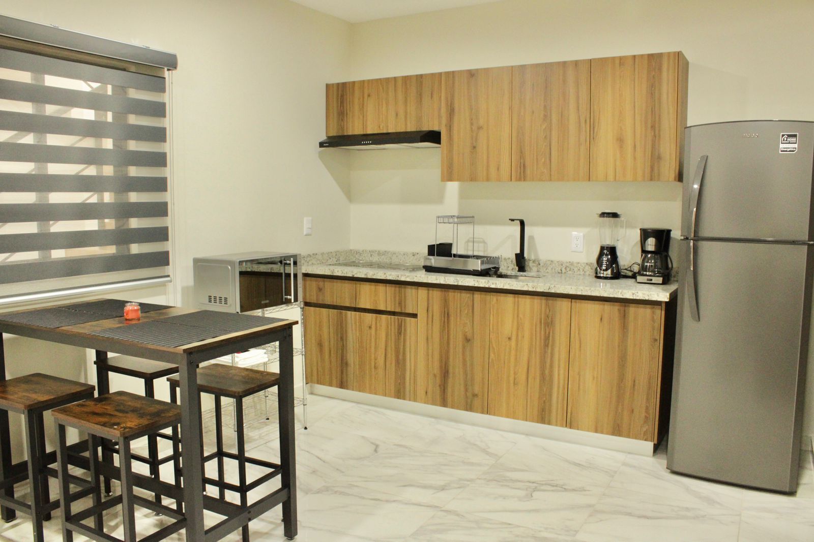 A compact kitchen with wooden cabinets, a stainless steel refrigerator, a coffee maker, and a microwave.