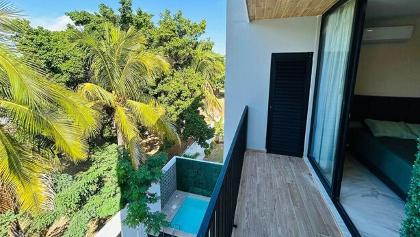 Un balcón con piscina, cama y vista a árboles tropicales.