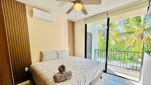 Un dormitorio con cama, ventilador de techo, ventana con vista a zonas verdes y balcón.