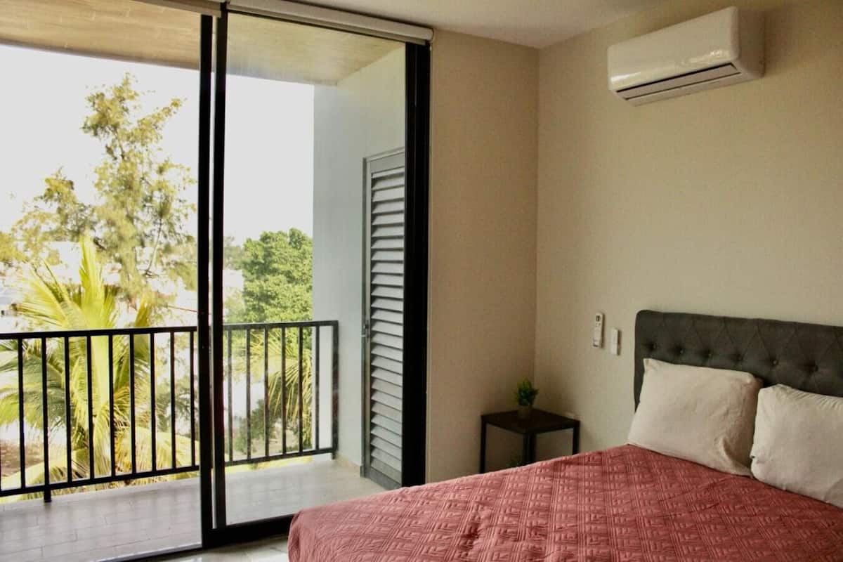 A bedroom with a bed, a nightstand, and a view of a balcony with a railing.