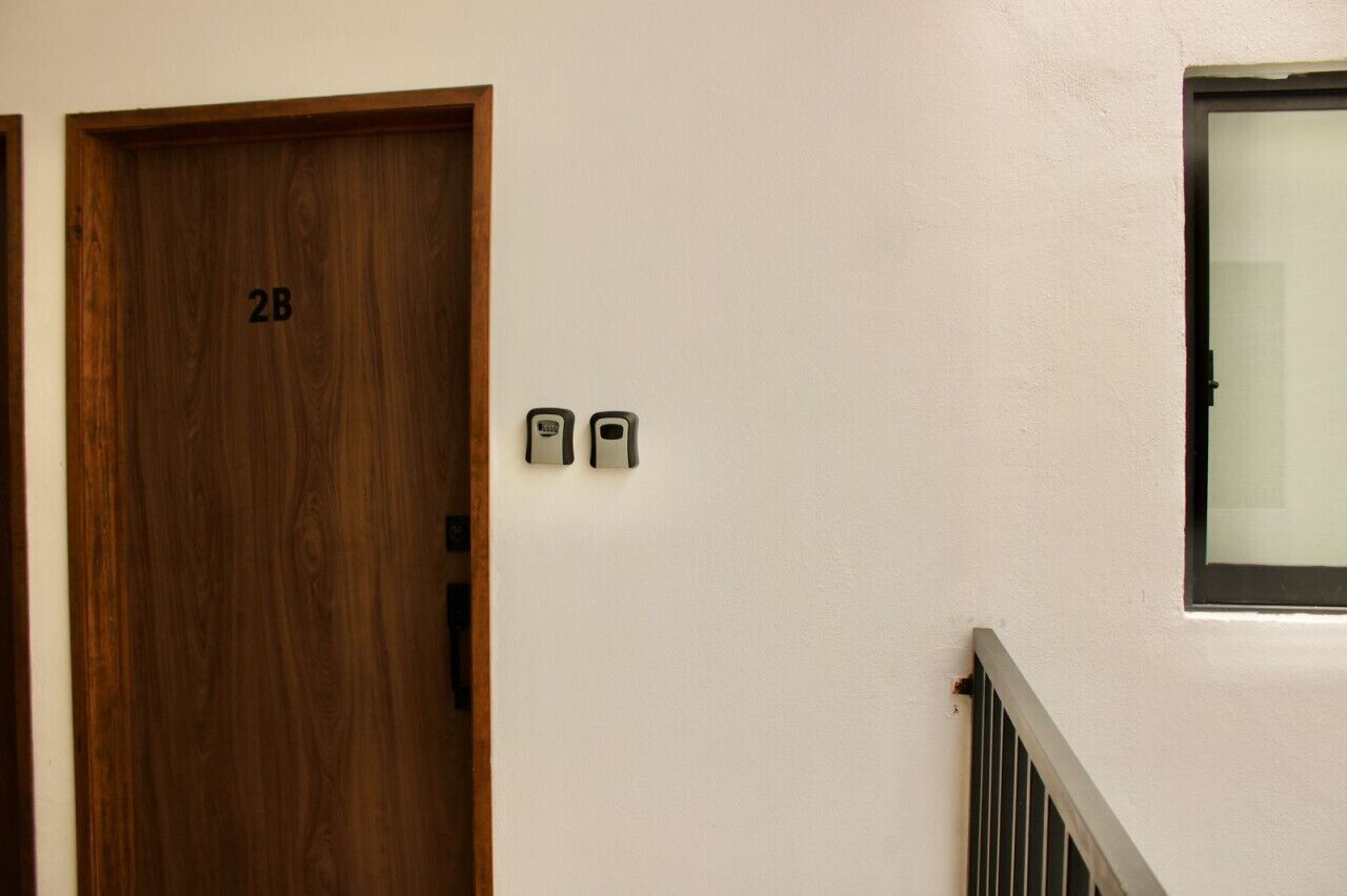 Una puerta de madera con una placa de identificación '2B' y dos dispositivos de intercomunicación fijados en la pared.