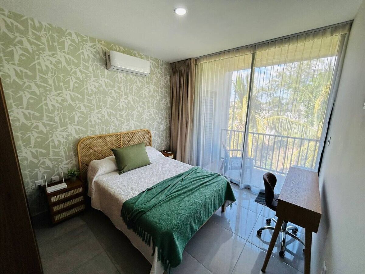 A bedroom with a bed, a desk, and a window with curtains.