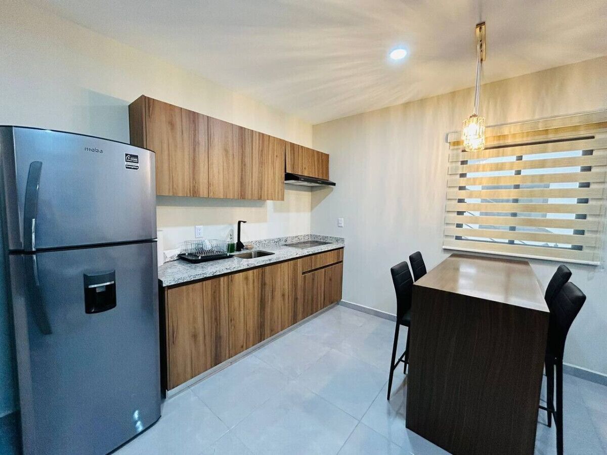 A modern kitchen with wooden cabinets, a stainless steel refrigerator, a granite countertop, and a bar area with stools.
