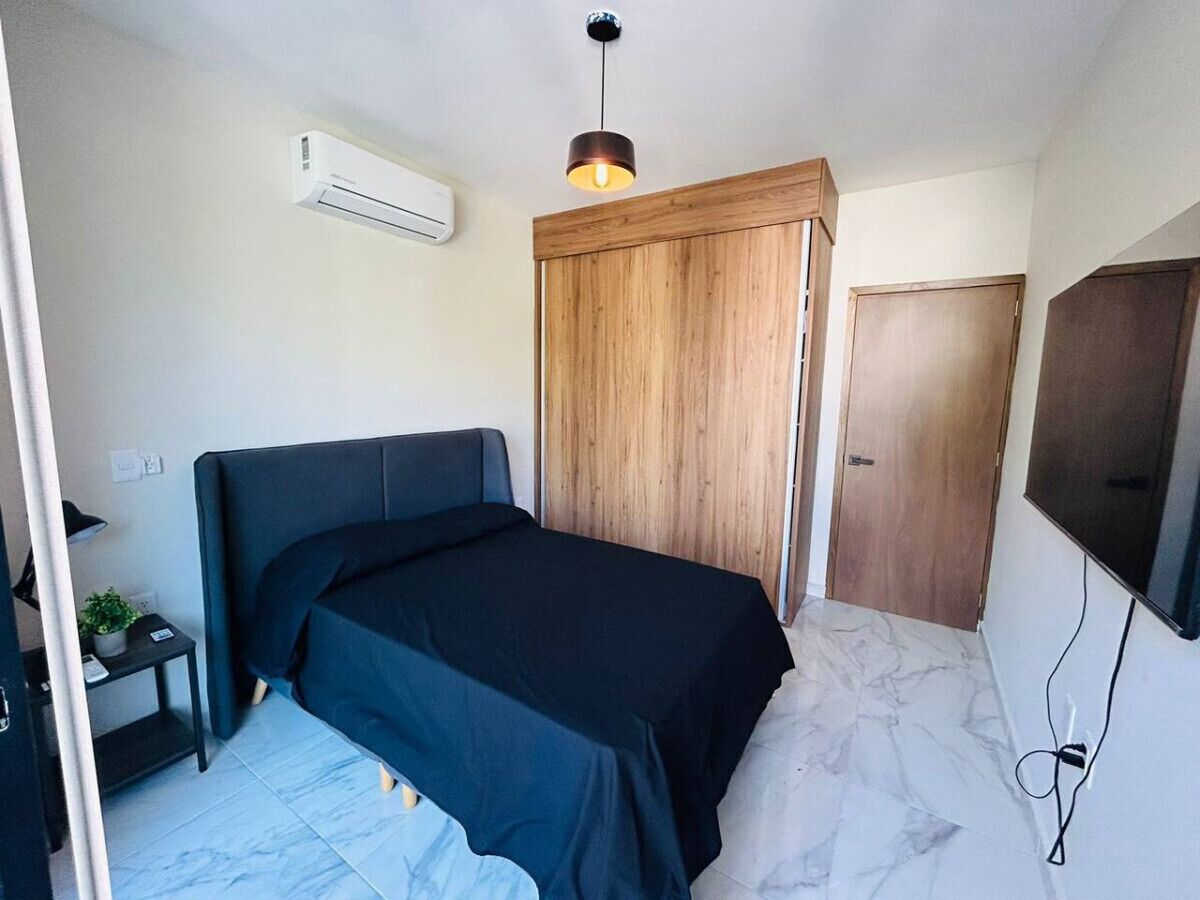 Un dormitorio con cama, armario de madera, televisor y aire acondicionado.