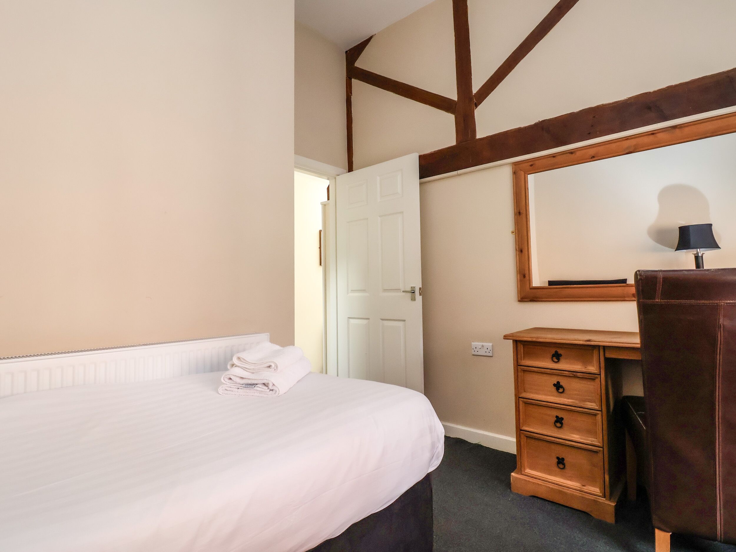Quarto com cama, cómoda de madeira, espelho e porta.