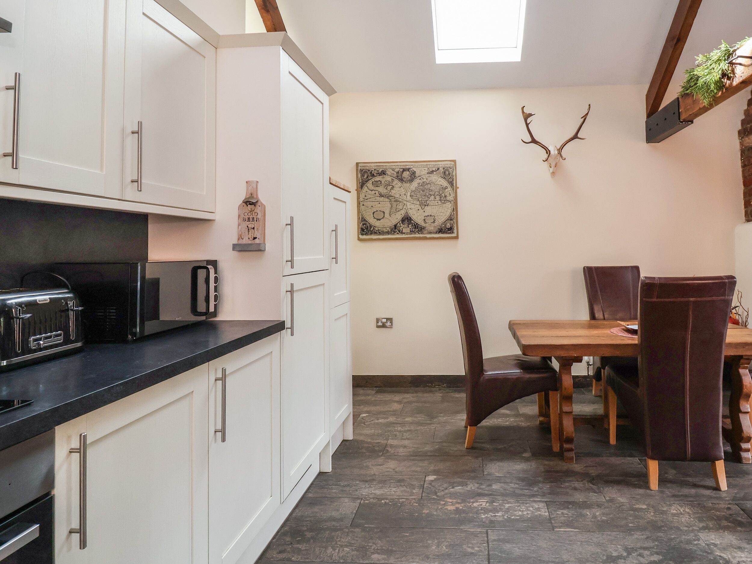 A kitchen with white cabinets, a black countertop, a toaster, and a microwave. There is a dining table with chairs and a wall-mounted globe.