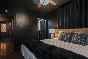 Un dormitorio con cama, ventilador de techo, mesita de noche y una puerta.