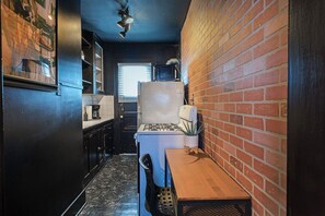 Una cocina estrecha con pared de ladrillo, estufa a gas, microondas y una pequeña mesa de comedor.