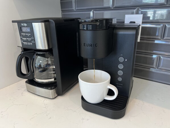 Una cafetera con pantalla digital y depósito de agua, conectada a un dispensador de café de goteo.