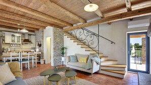 A spacious living area with a wooden ceiling, a staircase with a metal railing, a sofa, a dining table, and a kitchen in the background. - Villa Runka (Istria - Muntic) (Muntic)