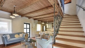 A spacious living area with a wooden staircase, a sofa, a dining table, and a kitchen in the background. - Villa Runka (Istria - Muntic) (Muntic)