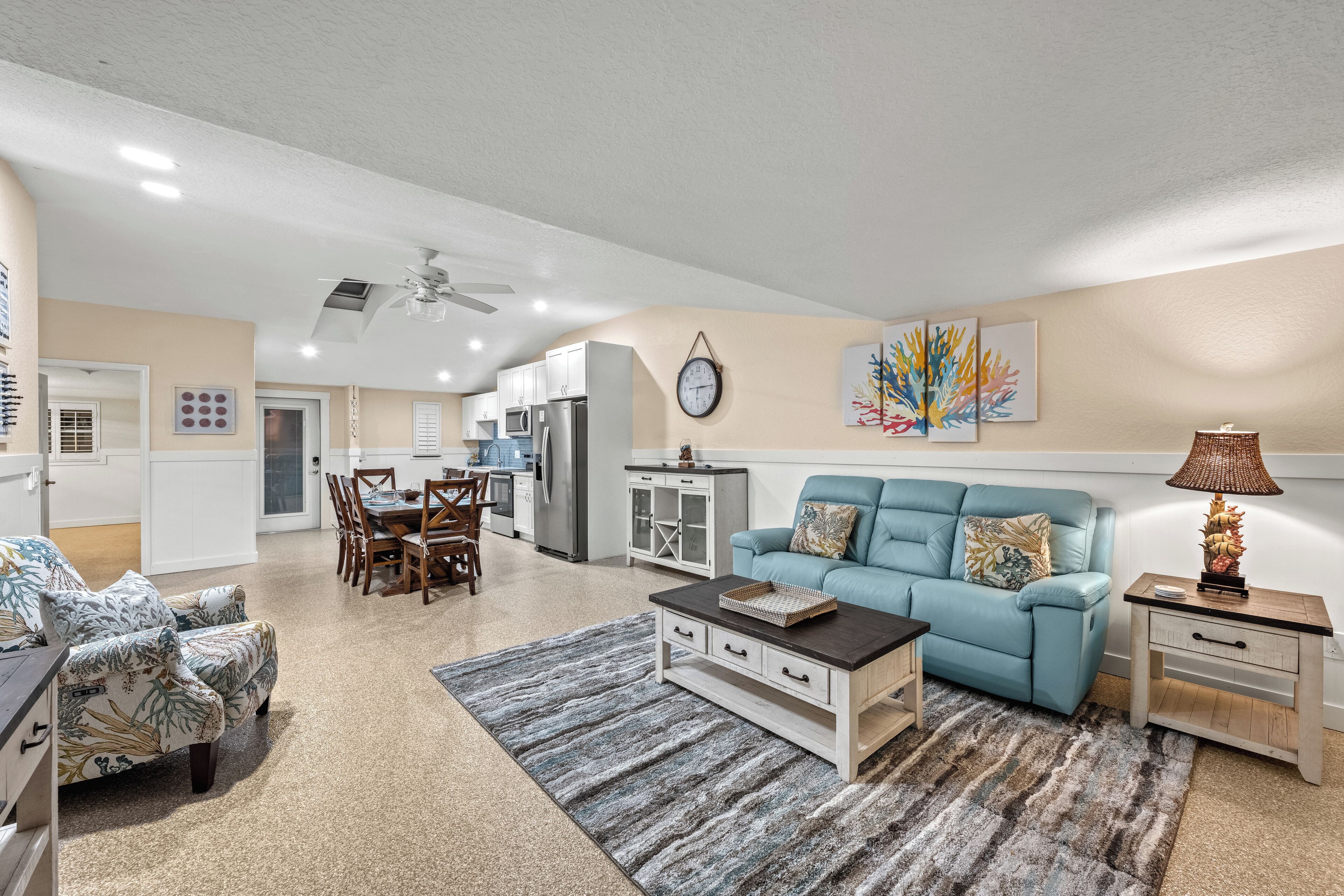 A spacious living room with a blue sofa, a coffee table, and a dining area with a table and chairs.
