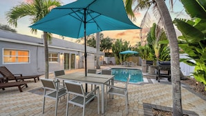 Eine Terrasse mit Pool, Gartenmöbeln und einem türkisblauen Sonnenschirm.