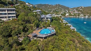 A resort with a pool surrounded by lush greenery, overlooking a clear blue sea.