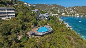A resort with a pool surrounded by lush greenery, overlooking a clear blue sea.