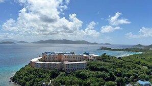A resort with multiple buildings surrounded by lush greenery and a clear view of the ocean.