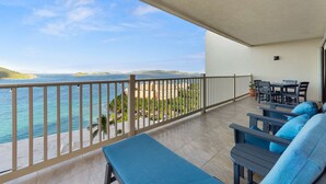 A balcony with a view of the sea and buildings, a table with chairs, and a blue sofa.