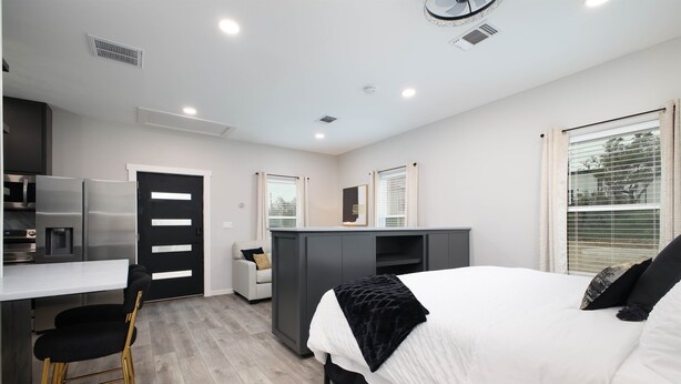 A modern bedroom with a bed, a desk, and a kitchenette.
