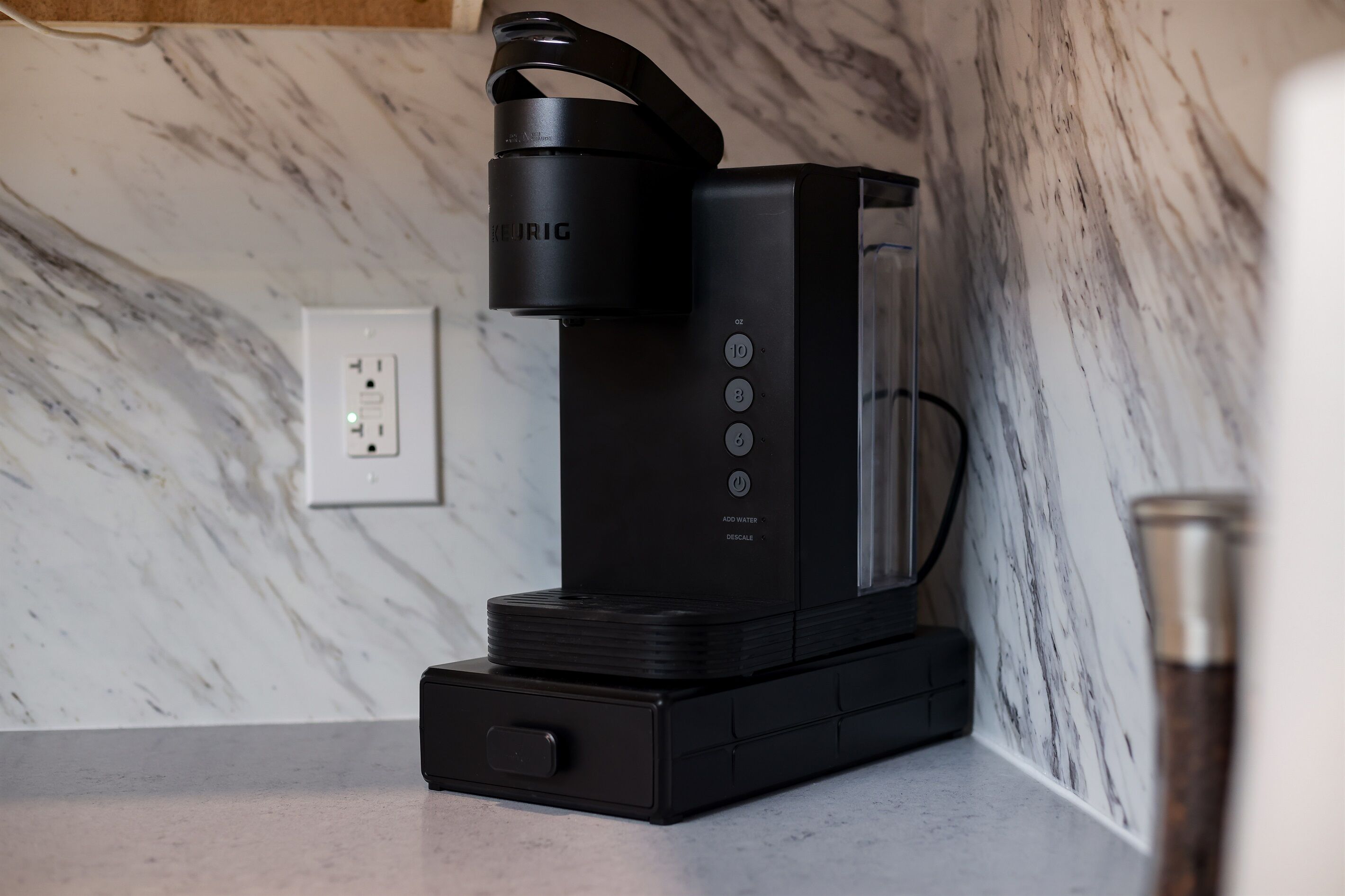 A black coffee machine with a water reservoir, control buttons, and a power cord on a marble countertop.
