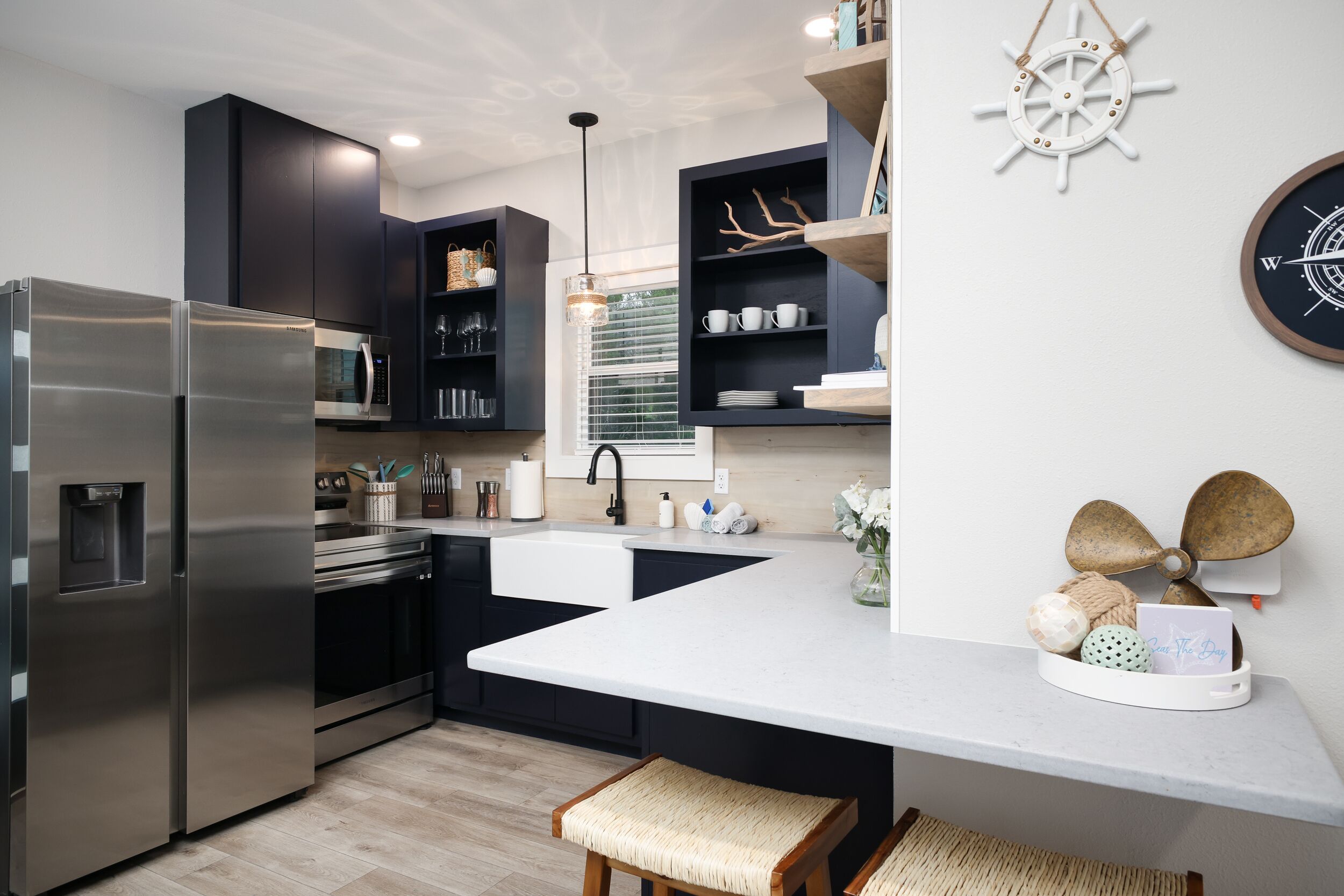 A modern kitchen with dark cabinetry, stainless steel appliances, a white countertop, and nautical decor.