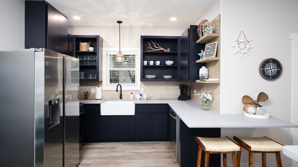 A modern kitchen with dark cabinetry, a stainless steel refrigerator, a white countertop, and wooden stools. - Serene Hill Country Casita ~ Scenic View ~ Patio (Spring Branch)
