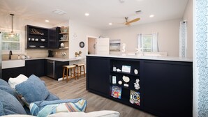 A modern kitchen with dark cabinetry, a white countertop, and a dining area with wooden stools. - Serene Hill Country Casita ~ Scenic View ~ Patio (Spring Branch)