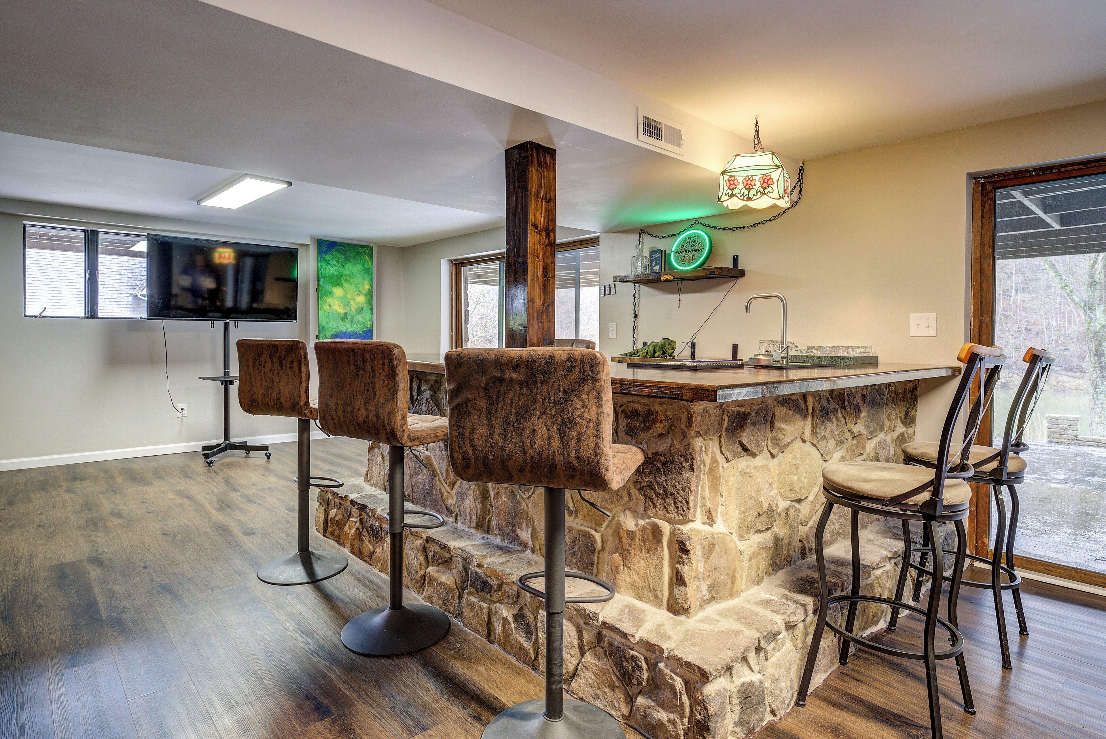 Une cuisine avec un îlot central en pierre, des tabourets de bar, un téléviseur et une fenêtre.