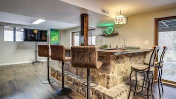 Une cuisine avec un îlot central en pierre, des tabourets de bar, un téléviseur et une fenêtre.