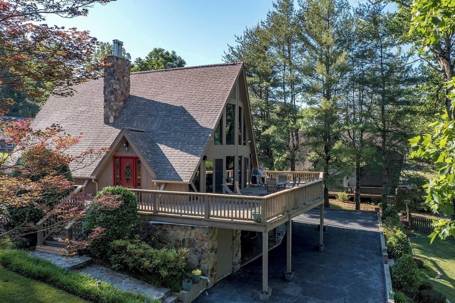 Une maison à deux étages avec un balcon, une cheminée en pierre et une porte rouge.