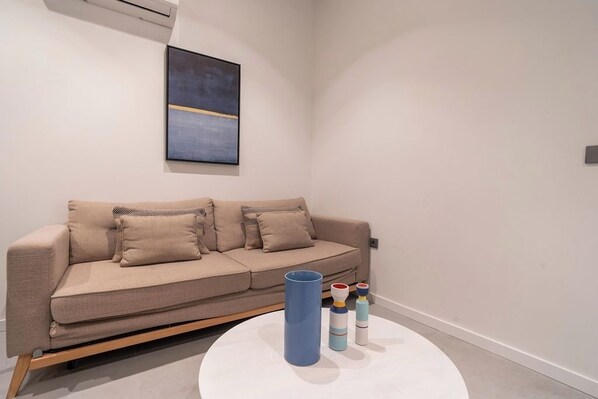 A modern living room with a beige sofa, a round white coffee table, and a minimalist abstract painting on the wall.