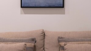 Ein Zimmer mit einem beigen Sofa, gemusterten Kissen, einem gerahmten abstrakten Gemälde an der Wand und einer schlichten weißen Wand.
