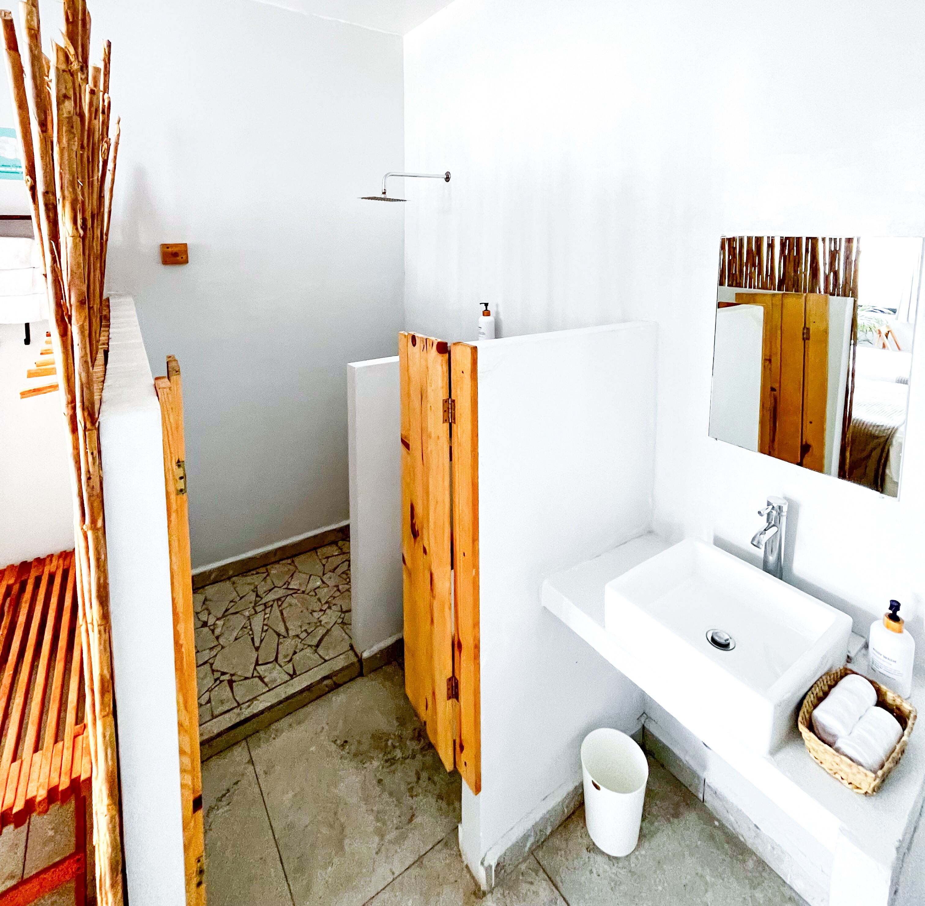 Un baño con lavamanos blanco, espejo y zona de ducha.