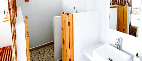 Un baño con lavamanos blanco, espejo y zona de ducha.