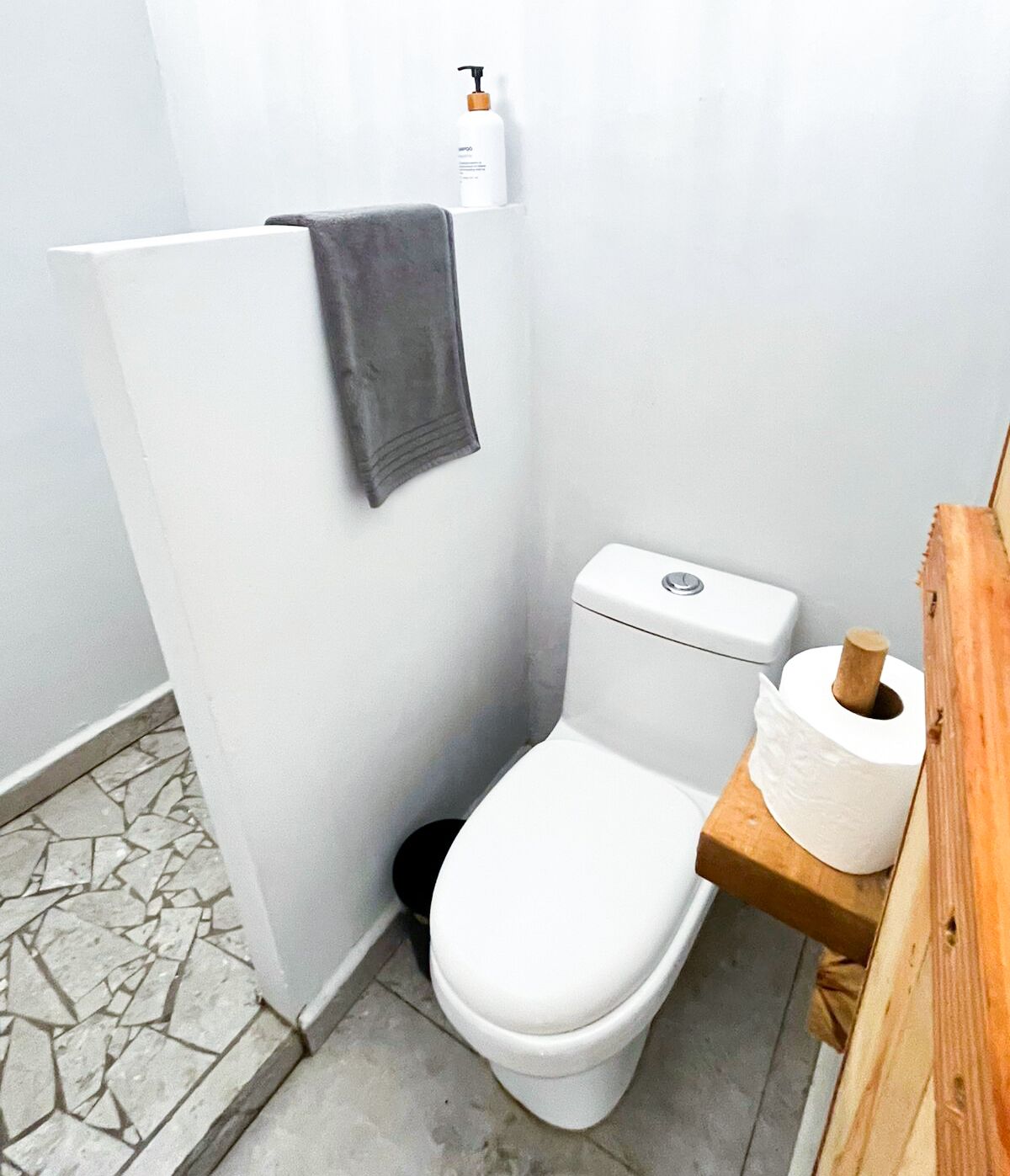 Een kleine, praktische badkamer met een wit toilet, een houten plankje met een toiletrol en een handdoek aan de muur.