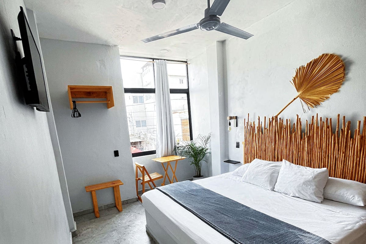 A modern hotel room with a large bed, a ceiling fan, a small table, and a chair.