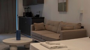 Een moderne, minimalistisch ingerichte hotelkamer met een beige bank, een ronde tafel met een blauwe vaas, en een netjes opgemaakt bed.