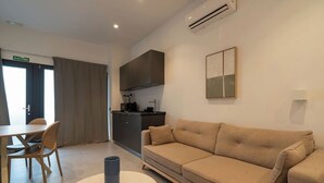 Een moderne woonkamer met een bank, een eettafel met stoelen, een keukenhoek en een airconditioner.