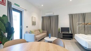 Ett modernt hotellrum med en soffa, en TV, en säng, ett matbord och ett litet sidobord.
