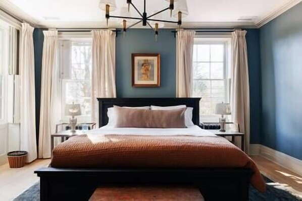 A bedroom with a large bed, a chandelier, and a painting on the wall.