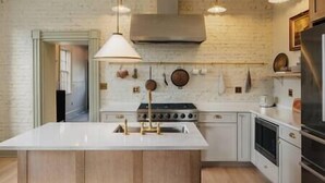 A modern kitchen with a central island, white cabinetry, and a brick wall. - Serene Estate: Heated Pool, Tennis, Sauna, Hot Tub (Catskill)