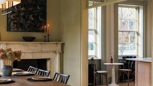 A dining area with a fireplace, a table set for two, and a view of the outside through large windows. - Serene Estate: Heated Pool, Tennis, Sauna, Hot Tub (Catskill)