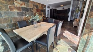 Un coin repas avec une table en bois et des chaises en cuir noir, un vase orné de feuillage vert et un mur en pierre.